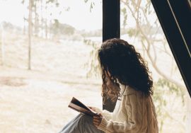 Frau auf Holzboden vor Fenster liest ein Buch