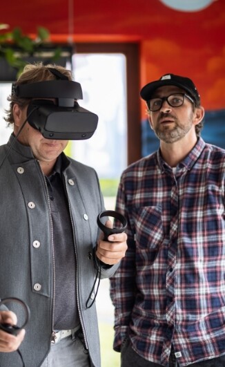 Zwei Männer stehen nebeneinander einer davon hat eine VR Brille aufgesetzt